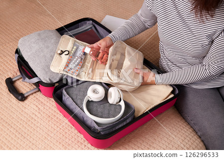 A woman puts hygiene products, clothes, a travel guide, headphones and travel accessories in a suitcase A woman puts hygiene products, clothes, a travel guide, headphones and travel accessories in a suitcase 126296533