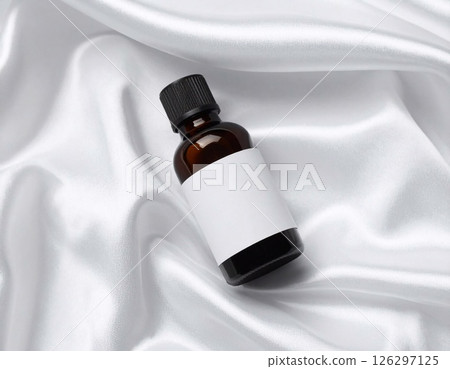 photograph of a dark amber oil bottle resting elegantly on a pristine white silk photograph of a dark amber oil bottle resting elegantly on a pristine white silk 126297125