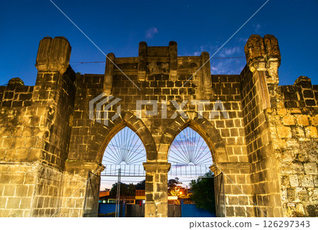 Entrance Gate of Mercado de Artesanias or craft market of Masaya in Nicaragua features Gothic-inspired pointed arches and crenellated battlements lit by soft evening lamps, framing a twilight sky over Entrance Gate of Mercado de Artesanias or craft market of Masaya in Nicaragua features Gothic-inspired pointed arches and crenellated battlements lit by soft evening lamps, framing a twilight sky over 126297343