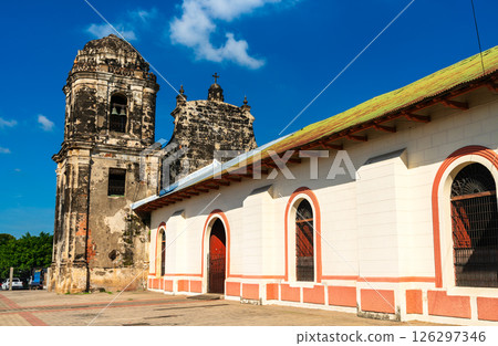 San Juan Church rises beneath a clear blue sky in the heart of Leon, Nicaragua. Its weathered stone bell tower and contrasting freshly painted facade reflect centuries of colonial history and 126297346