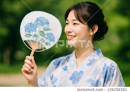 一位身穿藍色浴衣的年輕女子微笑著，手裡拿著一把扇子 126298362