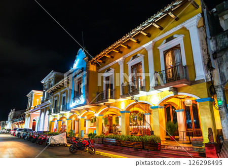 A historic colonial-era building with arched porticoes and balconies glows under streetlights at the Central Park of Granada, Nicaragua. The nighttime setting highlights the rich yellow facade and A historic colonial-era building with arched porticoes and balconies glows under streetlights at the Central Park of Granada, Nicaragua. The nighttime setting highlights the rich yellow facade and 126298495