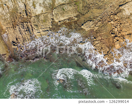 Aerial top down view of ocean waves crashing into rocky shore 126299014