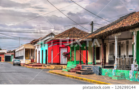 Row of vibrant colonial-style houses with ornate balconies, arched windows, and lush greenery lines a narrow cobblestone street in Granada, Nicaragua. The pastel colors and architectural details 126299144