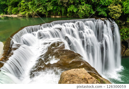 Shifen Waterfall in Pingxi District of New Taipei, Taiwan, cascades powerfully into a turquoise pool amid dense green foliage, offering a scenic and tranquil natural attraction often called the Little Shifen Waterfall in Pingxi District of New Taipei, Taiwan, cascades powerfully into a turquoise pool amid dense green foliage, offering a scenic and tranquil natural attraction often called the Little 126300059