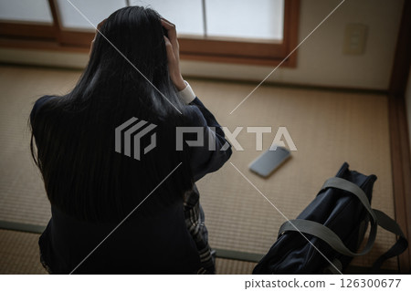 High school girl looking at smartphone placed on tatami mat in Japanese-style room Bullying, truancy, SNS troubles, out of focus person 126300677