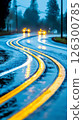 Curved road illuminated by headlights on a rainy evening with reflections in puddles 126300785