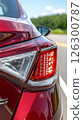 Close-up view of a red car's taillight on a sunny day along a rural road 126300787