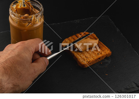 Peanut butter spread on toasted bread with a knife 126301017