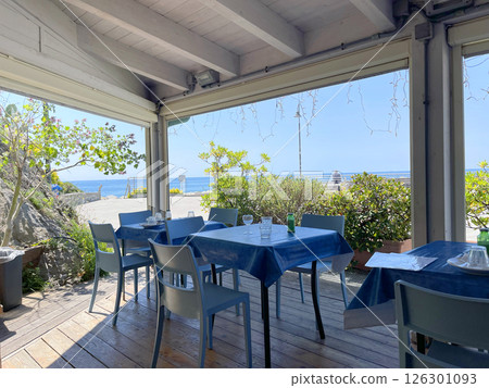 Tables set with blue tablecloths in outdoor cafe under canopy near sea. Food and relaxation. Nature and enjoyment. 126301093