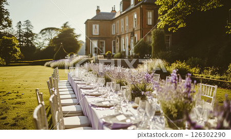 Elegant outdoor dining table set for a celebration in a beautiful garden with a historic building backdrop and purple lavender bushes. 126302290