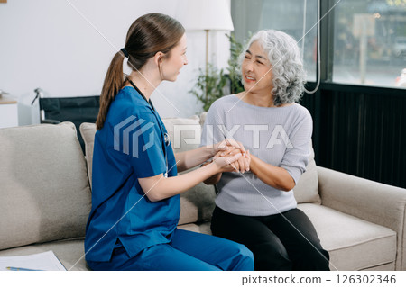 Young nurse helping elderly woman walk in the room, holding his hand, supporting. Treatment and rehabilitation after injury in assisted living facility Young nurse helping elderly woman walk in the room, holding his hand, supporting. Treatment and rehabilitation after injury in assisted living facility 126302346