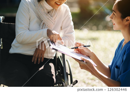 Elderly asian senior woman on wheelchair with Asian careful caregiver and encourage patient, walking in garden. with care from a caregiver. and senior health insurance 126302446