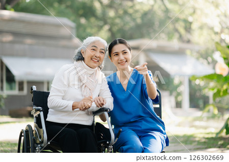 Elderly asian senior woman on wheelchair with Asian careful caregiver and encourage patient, walking in garden. with care from a caregiver Elderly asian senior woman on wheelchair with Asian careful caregiver and encourage patient, walking in garden. with care from a caregiver 126302669