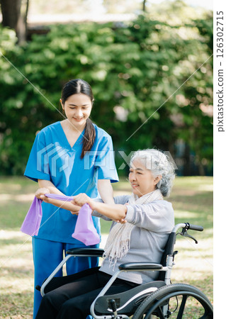 Asian physiotherapist helping elderly woman patient stretching arm during exercise correct with dumbbell in hand during training hand with patient Back problems in the garden. 126302715