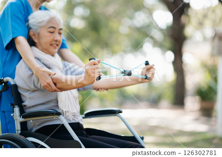 Asian physiotherapist helping elderly woman patient stretching arm during exercise correct with dumbbell in hand during training hand with patient Back problems in the garden. Asian physiotherapist helping elderly woman patient stretching arm during exercise correct with dumbbell in hand during training hand with patient Back problems in the garden. 126302781