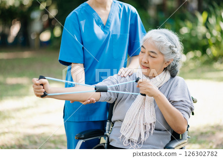Asian physiotherapist helping elderly woman patient stretching arm during exercise correct with dumbbell in hand during training hand with patient Back problems in the garden. Asian physiotherapist helping elderly woman patient stretching arm during exercise correct with dumbbell in hand during training hand with patient Back problems in the garden. 126302782