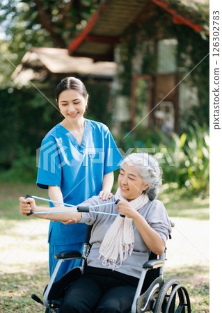 Asian physiotherapist helping elderly woman patient stretching arm during exercise correct with dumbbell in hand during training hand with patient Back problems in the garden. Asian physiotherapist helping elderly woman patient stretching arm during exercise correct with dumbbell in hand during training hand with patient Back problems in the garden. 126302783