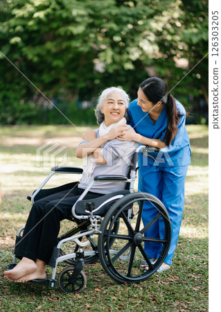 Elderly asian senior woman on wheelchair with Asian careful caregiver and encourage patient, walking in garden. with care from a caregiver and senior health insurance. Elderly asian senior woman on wheelchair with Asian careful caregiver and encourage patient, walking in garden. with care from a caregiver and senior health insurance. 126303205