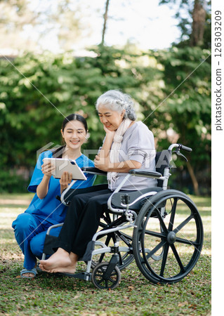 Elderly asian senior woman on wheelchair with Asian careful caregiver and encourage patient, walking in garden. with care from a caregiver and senior health insurance. Elderly asian senior woman on wheelchair with Asian careful caregiver and encourage patient, walking in garden. with care from a caregiver and senior health insurance. 126303209