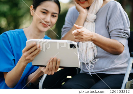 Elderly asian senior woman on wheelchair with Asian careful caregiver and encourage patient, walking in garden. with care from a caregiver and senior health insurance. 126303212