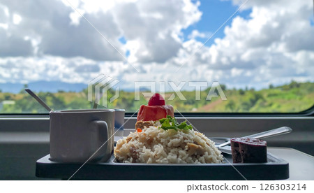 A meal is served on a tray inside a train with a scenic view of the landscape outside the window. A meal is served on a tray inside a train with a scenic view of the landscape outside the window. 126303214