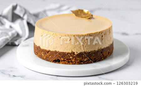A layered no-bake cake with a nut crust and creamy top, adorned with a golden leaf, on a marble board. 126303219