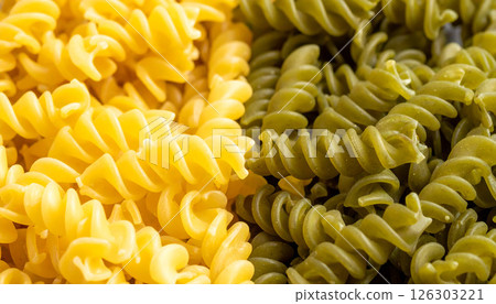 A macro close-up of yellow and green spiral pasta, showing the details and textures of the uncooked fusilli noodles. 126303221