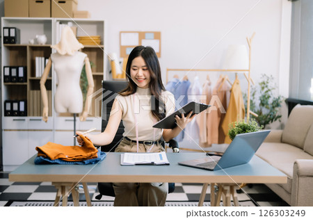 Asian young woman on desk in office of fashion designer and holds tablet, laptop and smartphone on desk Asian young woman on desk in office of fashion designer and holds tablet, laptop and smartphone on desk 126303249