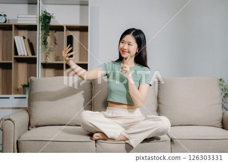 Young asian woman using smartphone and tablet while seated on couch at home Young asian woman using smartphone and tablet while seated on couch at home 126303331
