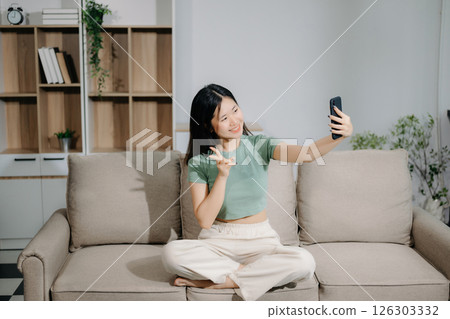 Young asian woman using smartphone and tablet while seated on couch at home 126303332