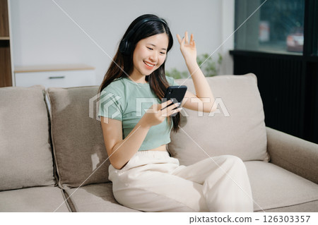 Young asian woman relax on comfortable couch at home texting messaging on smartphone and tablet smiling girl use cellphone shopping online Young asian woman relax on comfortable couch at home texting messaging on smartphone and tablet smiling girl use cellphone shopping online 126303357