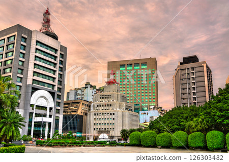 Skyline of Ximending district in Taipei, Taiwan during sunset, featuring a blend of modern and mid-century buildings framed by lush greenery and a colorful sky. Prominent towers rise above the dense 126303482