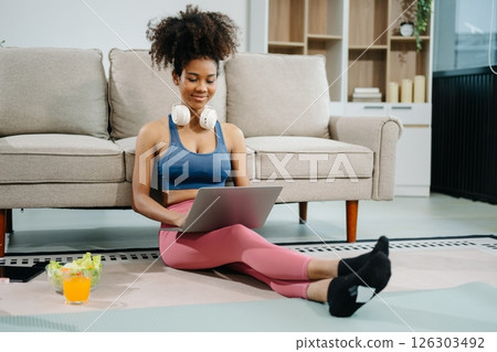 Active woman in athleisure sitting on yoga mat with tablet, headphones and modern home lifestyle. Active woman in athleisure sitting on yoga mat with tablet, headphones and modern home lifestyle. 126303492