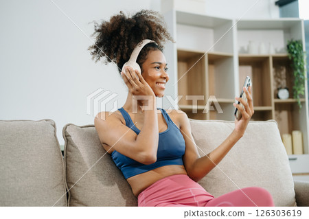 Active woman in athleisure sitting on yoga mat with tablet, headphones and modern home lifestyle. Active woman in athleisure sitting on yoga mat with tablet, headphones and modern home lifestyle. 126303619