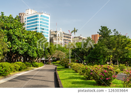 Lush garden path inside 228 Peace Memorial Park in Taipei, Taiwan, framed by blooming azaleas, manicured hedges, and dense trees with a backdrop of city buildings. This tranquil urban park 126303664