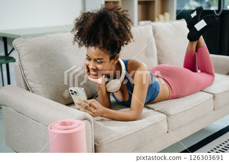 Active woman in athleisure sitting on yoga mat with tablet, headphones and modern home lifestyle. Active woman in athleisure sitting on yoga mat with tablet, headphones and modern home lifestyle. 126303691