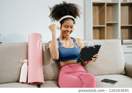 Active woman in athleisure sitting on yoga mat with tablet, headphones and modern home lifestyle. Active woman in athleisure sitting on yoga mat with tablet, headphones and modern home lifestyle. 126303695