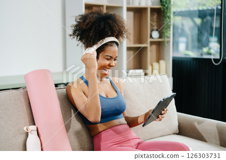 Active woman in athleisure sitting on yoga mat with tablet, headphones and modern home lifestyle. 126303731