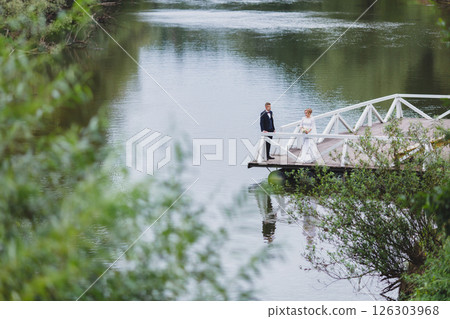 Beautiful newlywed couple in love posing on wooden pier with river in background 126303968