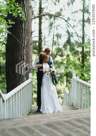 Beautiful newlywed couple in love posing on wooden stairs in summer park 126303980