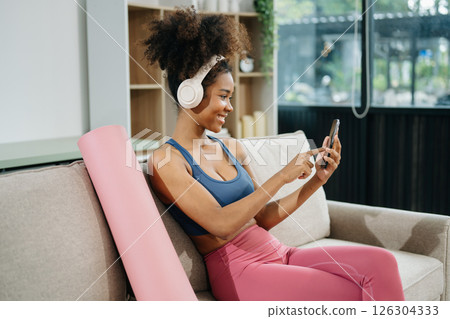 Active woman in athleisure sitting on yoga mat with tablet, headphones and modern home lifestyle. Active woman in athleisure sitting on yoga mat with tablet, headphones and modern home lifestyle. 126304333