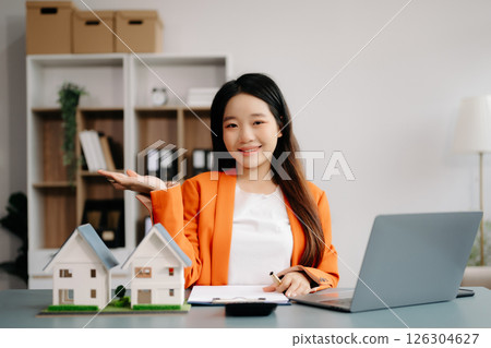 Young real estate agent worker working with laptop and tablet at table in office and small house beside it. 126304627
