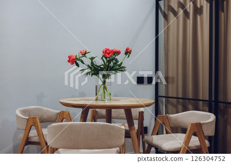 A beautiful arrangement of red peonies sits gracefully on a wooden table with accompanying chairs. A vibrant display of spring flowers in a glass vase 126304752
