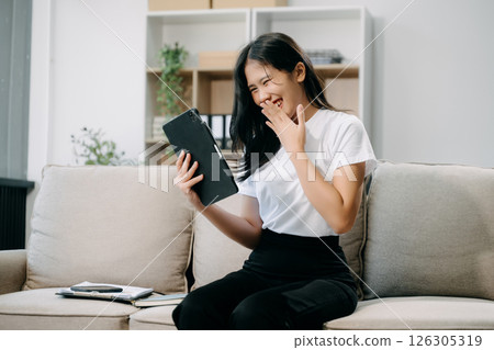 Young asian woman relax on comfortable couch at home texting messaging on smartphone and tablet smiling g Young asian woman relax on comfortable couch at home texting messaging on smartphone and tablet smiling g 126305319