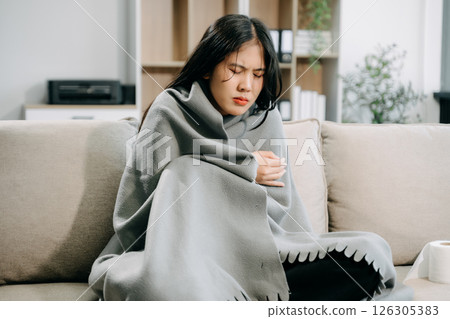 Young Asian woman suffering from flu symptoms, covered with a blanket on a sofa. Concept of illness, healthcare, Young Asian woman suffering from flu symptoms, covered with a blanket on a sofa. Concept of illness, healthcare, 126305383