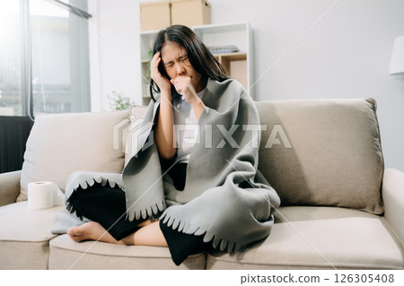 Young Asian woman suffering from flu symptoms, covered with a blanket on a sofa. Concept of illness, healthcare, Young Asian woman suffering from flu symptoms, covered with a blanket on a sofa. Concept of illness, healthcare, 126305408