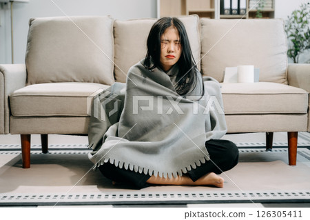Young Asian woman suffering from flu symptoms, covered with a blanket on a sofa. Concept of illness, healthcare, Young Asian woman suffering from flu symptoms, covered with a blanket on a sofa. Concept of illness, healthcare, 126305411