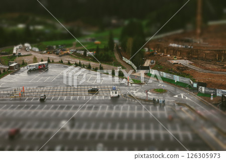 A parking lot, roads, construction site, and a bus in a blurred aerial view. A parking lot beside a road with cars, and a construction site nearby. 126305973