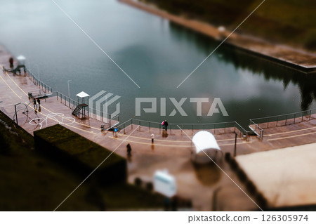 An aerial view showcases people near a tranquil lake, with a small dock and interesting shapes. The cloudy sky suggests a peaceful, serene atmosphere. 126305974